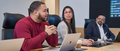 En person og en annen person som sitter ved et bord med bærbare datamaskiner