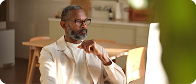 Um homem com barba e óculos sentado em uma sala.