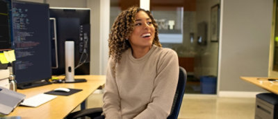 A person sitting in a chair near a desk with a computer screen and a yellow post-it note.
