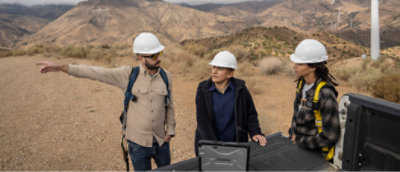 Drie personen die een helm dragen en naast een windturbine staan.