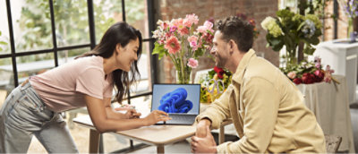 A man and woman sitting at a table looking at a laptop.