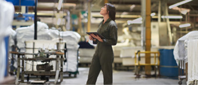A woman is standing in a factory holding a tablet.