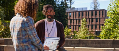 A person with a laptop in his hand talking to another person.