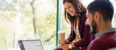 Eine Frau, die eine Kaffeetasse hält und auf einen Laptop schaut