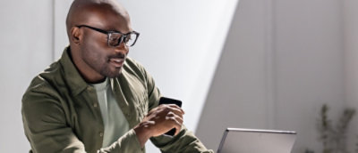 A man holding a phone and looking at a laptop.