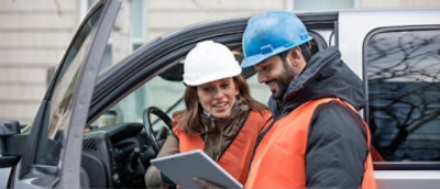 A man and woman wearing safety vests and hard hats looking at a tablet