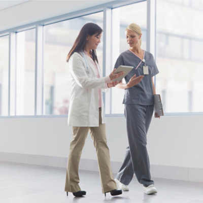 A woman in grey scrubs showing a tablet to a person in a white coat.
