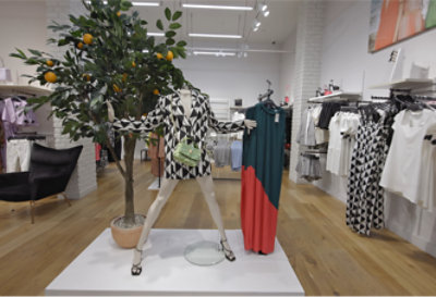 Een productdisplay in een kledingwinkel met een paspop naast een boom.