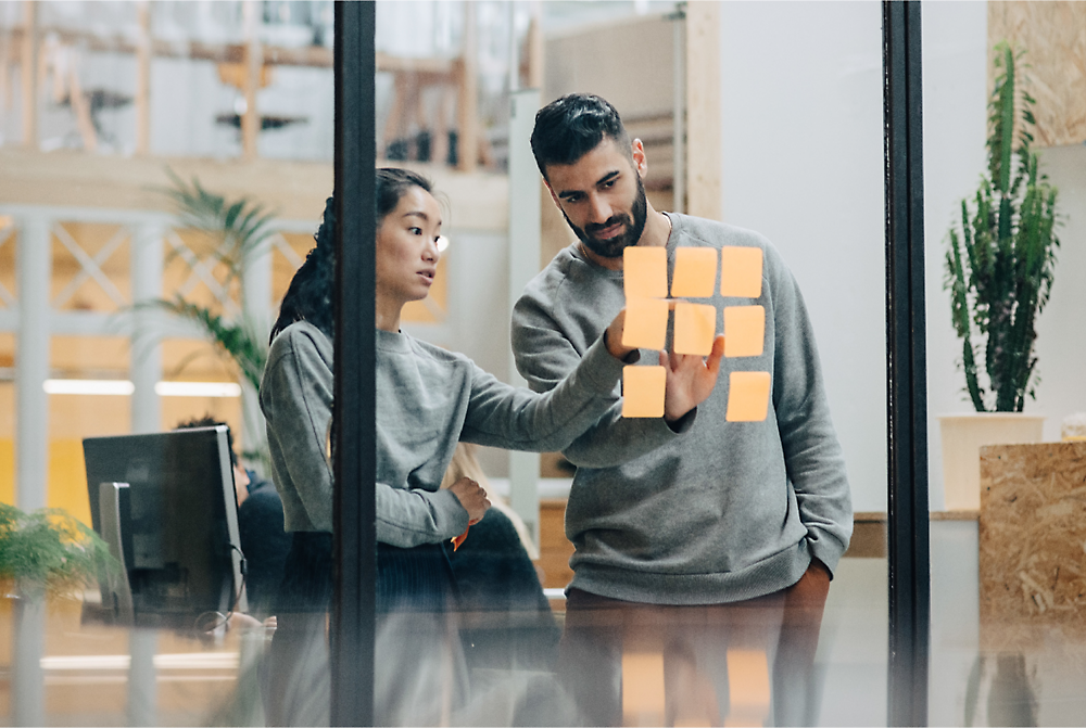Two people looking at sticky notes on a glass wall