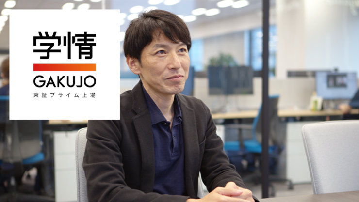 ダークジャケットとブルーのポロシャツを着た男性がオフィスに座っており、左側には「GAKUJO」のロゴと日本語の文字が入った白い四角があります。
