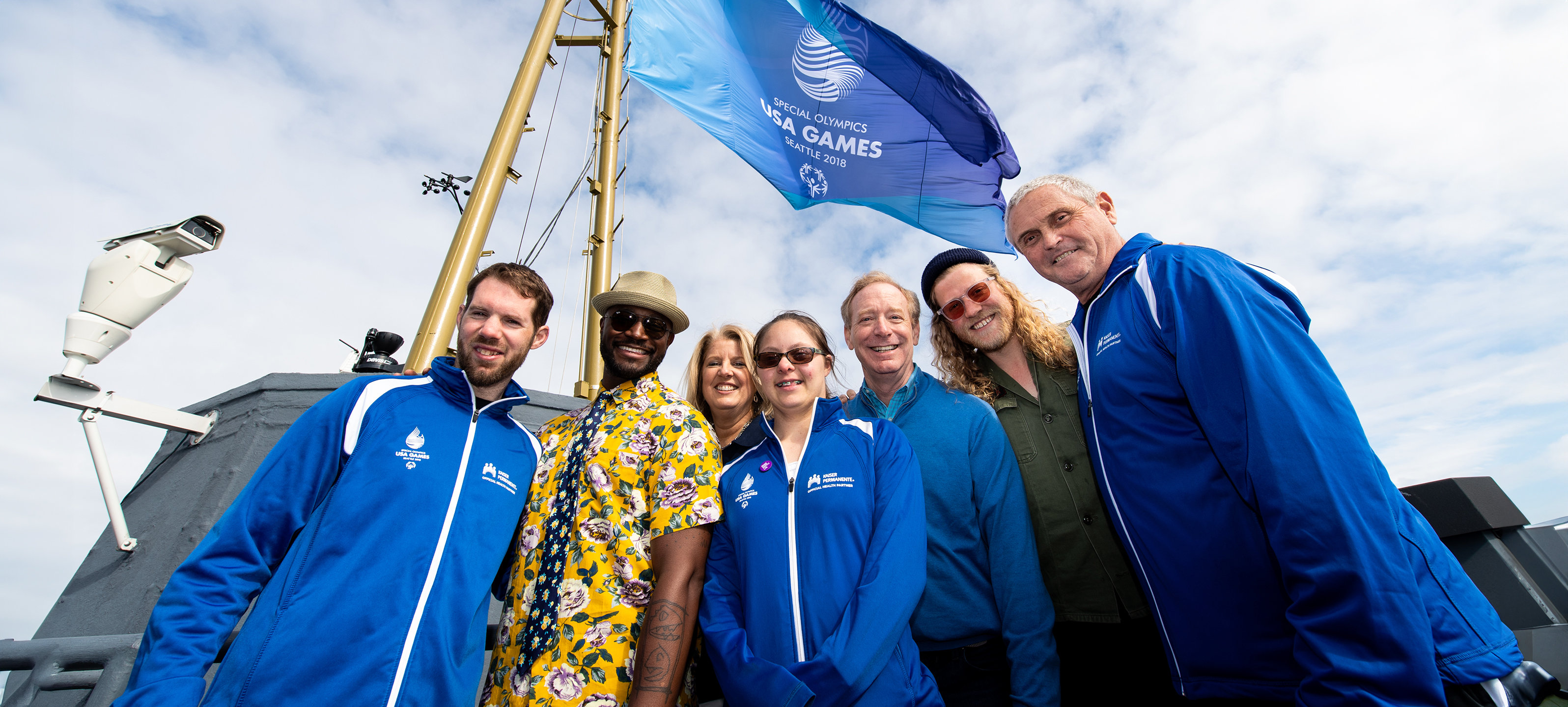 A group of people stand together, smiling, in front of a "Special Olympics USA Games" flag.