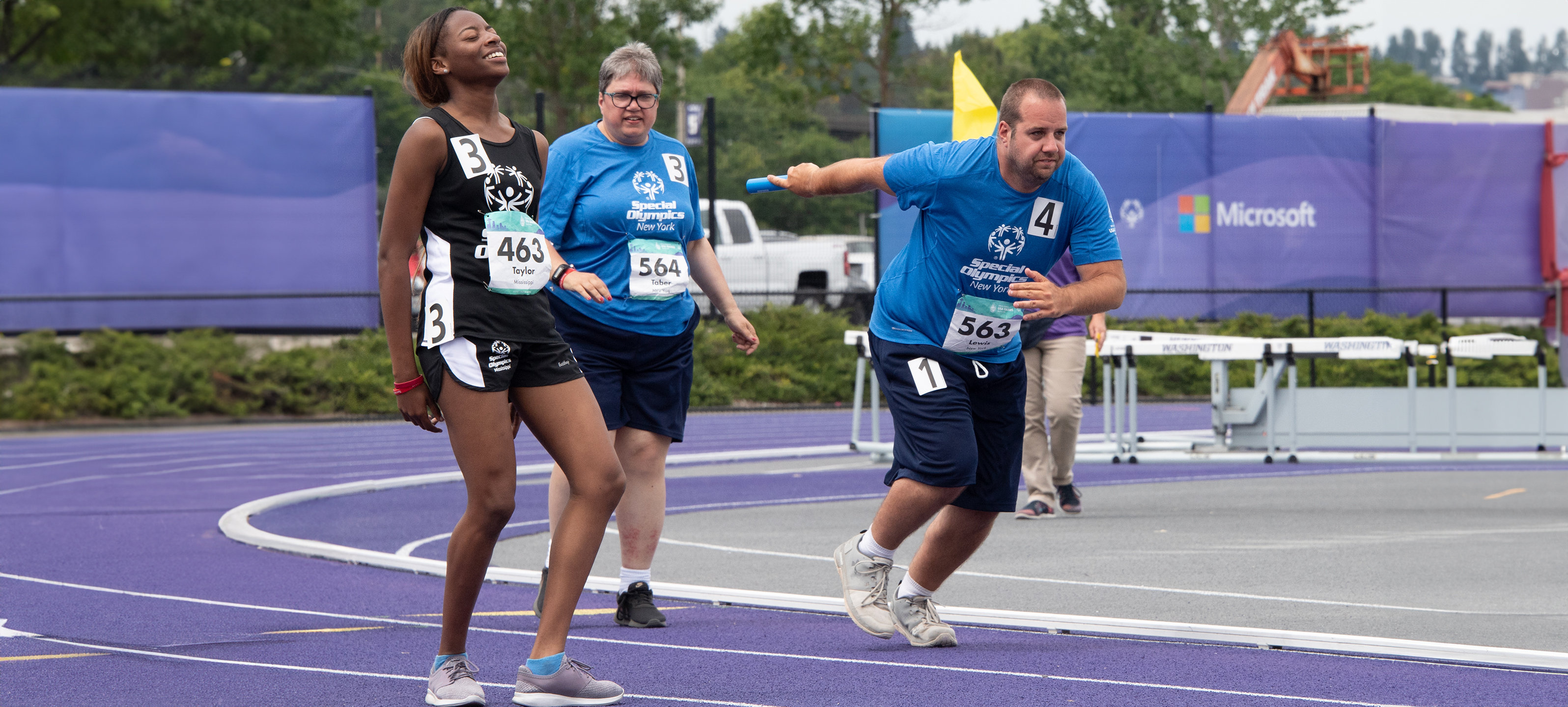 Three athletes participate in a relay race, where one runner prepares to pass the baton.