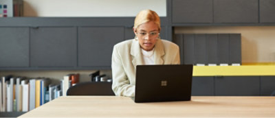 Person in a beige blazer working on a laptop at a modern office desk.
