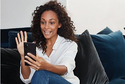 坐在沙發上使用行動電話參與視訊聊天的人