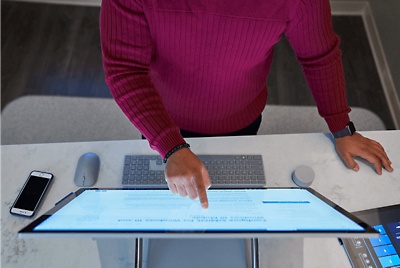 A top down view of a person standing at a desk using a touchscreen monitor