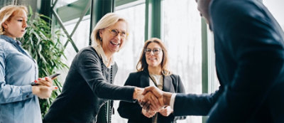 Grupa od tri osobe, dve žene i jedan muškarac, rukuju se u jarko osvetljenoj kancelariji, 