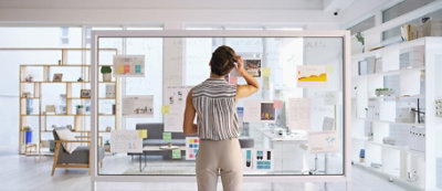 A person stands in front of a glass wall covered with notes and documents