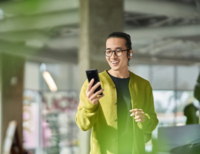 A man wearing glasses and a green cardigan holding a phone.