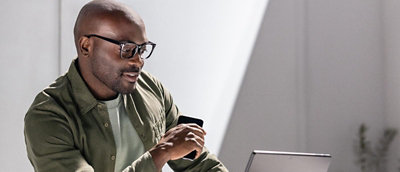 Person using a smartphone while working on a laptop at a desk.
