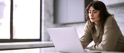 Person focused on a laptop, holding a smartphone while working at a desk