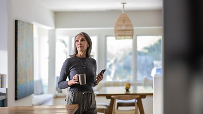 A women holding a teacup and mobile and looking some where.