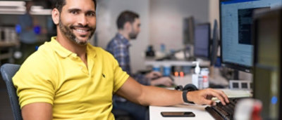A man smiling while sitting at desk with coworker in background