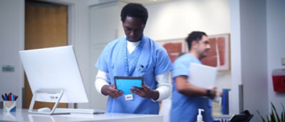 A man in blue scrubs holding a tablet.