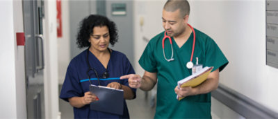 A man and woman in scrubs holding a folder and clipboard.