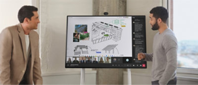 Two people stand near a digital whiteboard displaying a collaborative design diagram and a video call with participants.