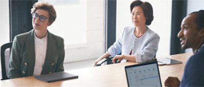 Three people sit at a conference table with laptops and notebooks.