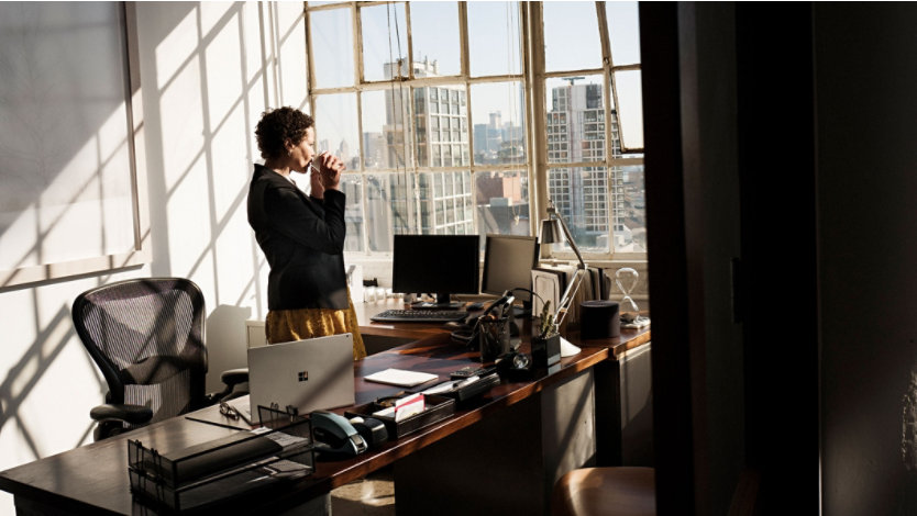 Une femme buvant dans une tasse et regardant par la fenêtre d’un bureau