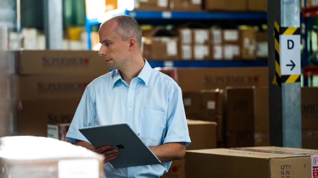 A person in a warehouse holding a tablet and looking at boxes