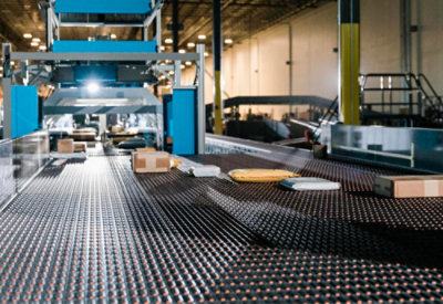 A conveyor belt carrying various packages in a warehouse, with machinery 
