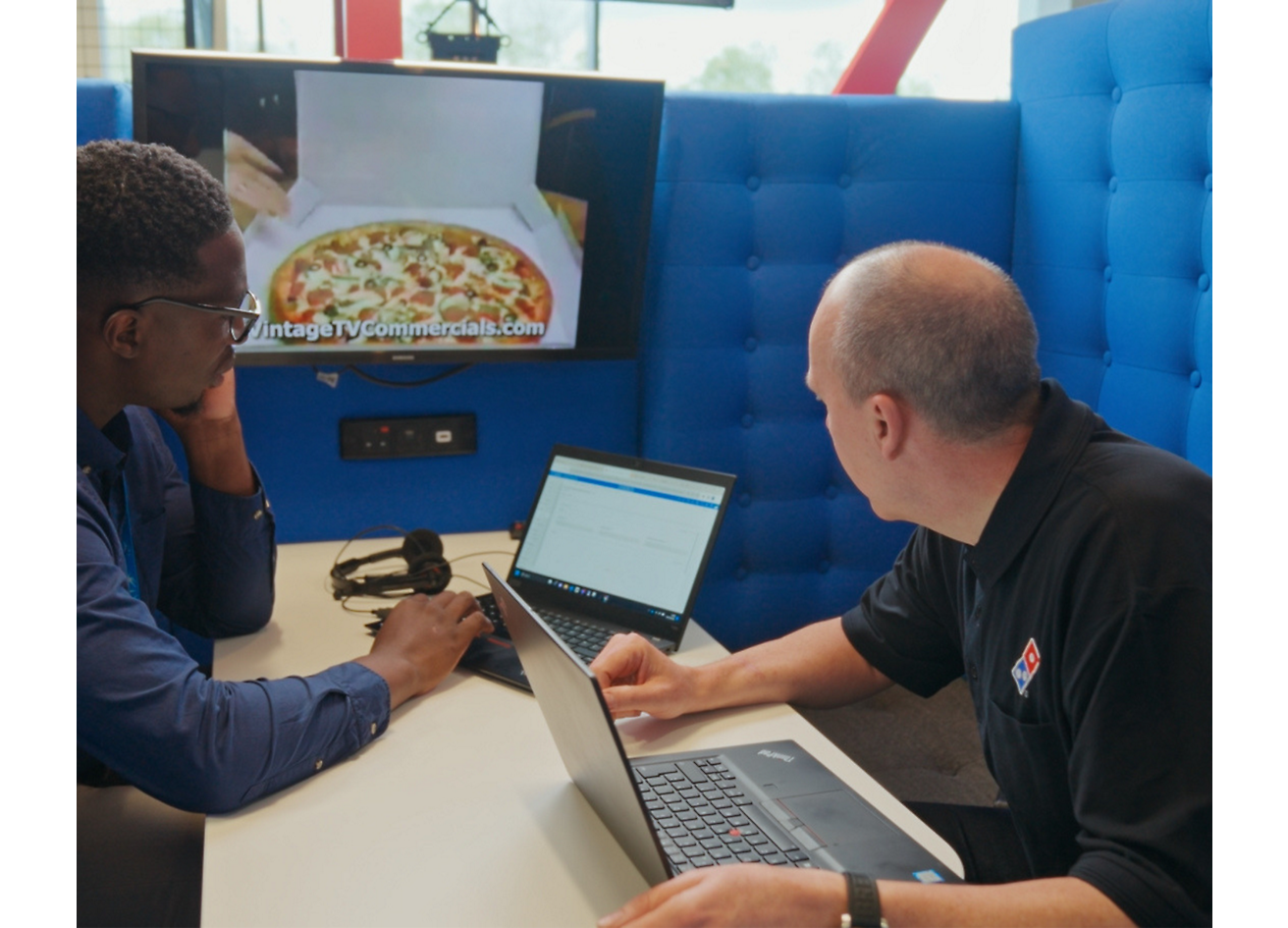 Два человека сидят с ноутбуком и обсуждают пиццу Dominos