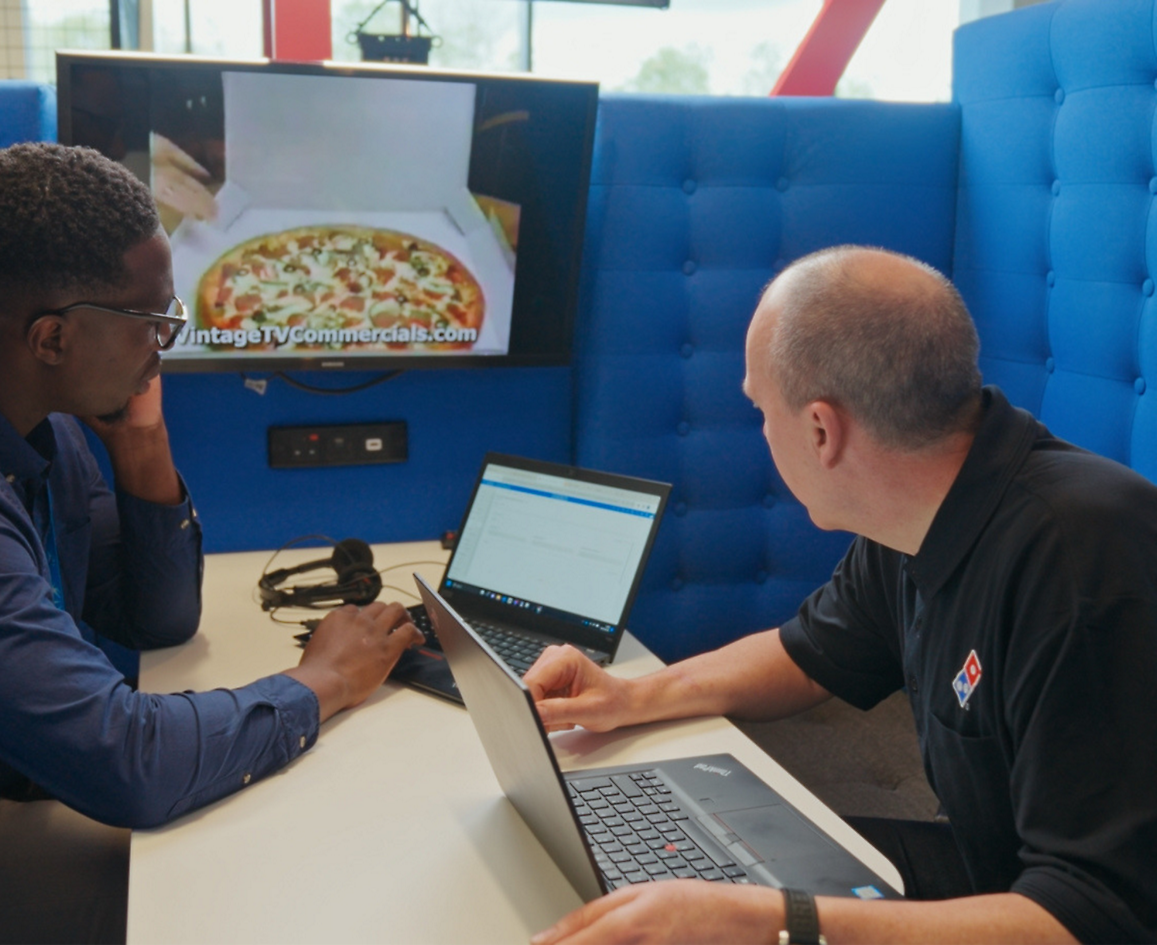 Duas pessoas sentadas com laptop e discutindo sobre a Domino's Pizza