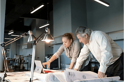 Two people working at a desk under lamp lights and looking at a tablet.