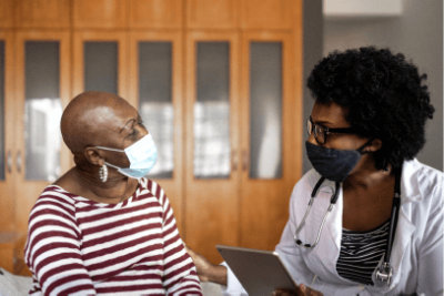 A healthcare professional and a patient wearing masks and having a conversation.