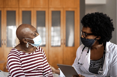 A healthcare professional and a patient wearing masks and having a conversation.