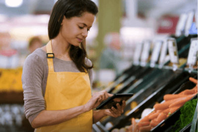 A grocery store employee using a tablet in the product department.