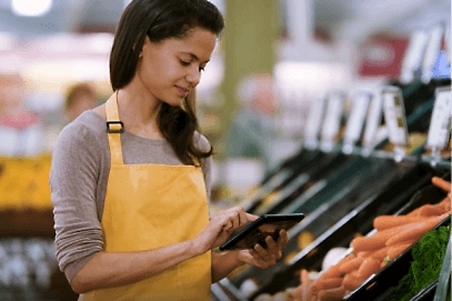 A grocery store employee using a tablet in the product department.