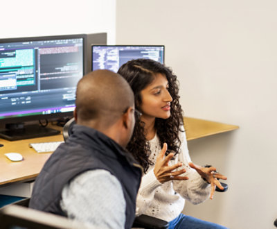 Two people sitting in front of a computer screen.