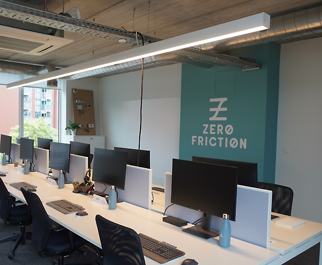 Kantor dengan beberapa meja dan monitor serta tanda dengan logo untuk Zero Friction