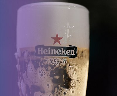Un bicchiere di birra Heineken su uno sfondo viola e nero.