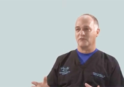 A person in medical scrubs is speaking against a plain background.
