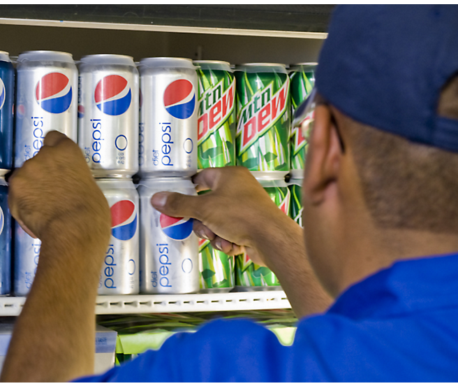 A man in a blue shirt picking up a can of pepsi.