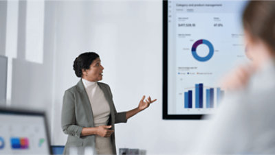 Egy személy adatokat mutat be a mögötte látható kijelzőn a munkatársainak