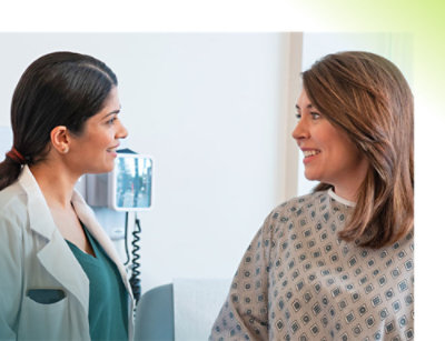 A woman in a hospital gown talking to a patient.