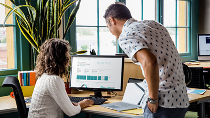 A girl sitting in front of a computer and explaining something to another person.