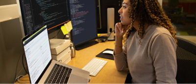 A woman with long curly hair looking at a computer screen with yellow sticky notes.