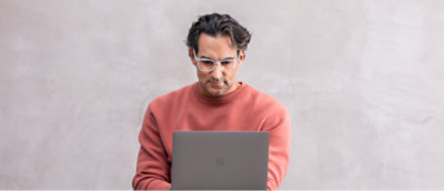 A man in glasses looking at a laptop.